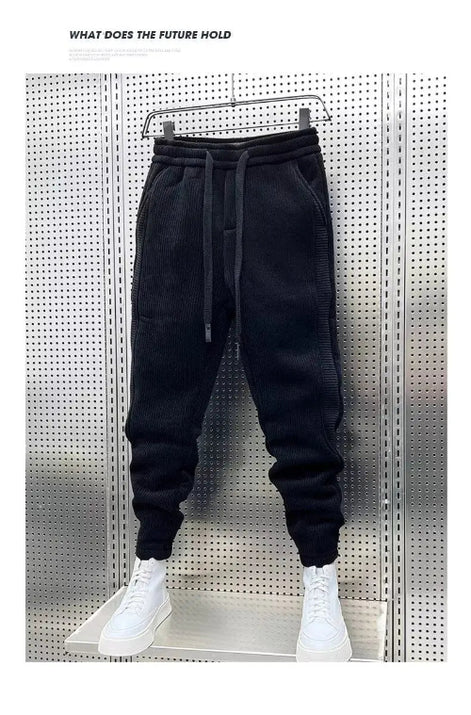 Black baggy sweatpants hanging on a hanger with white sneakers below and a white border around the photo.
