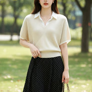A woman wearing a cream-colored short-sleeve knit polo sweater with a white collar, paired with a black polka-dot skirt and carrying a black shoulder bag.