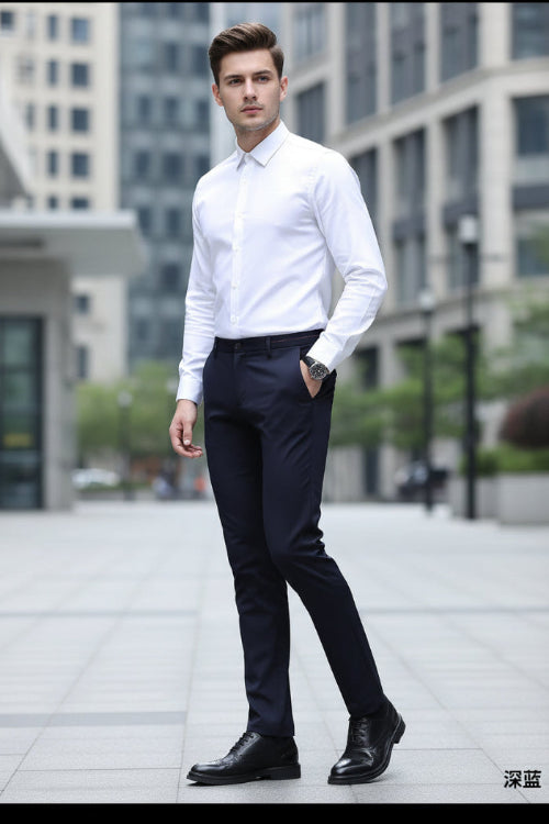 A man wearing slim-fit dark navy trousers, a white dress shirt, and black dress shoes, shown from the waist down against a dark gray studio background. 