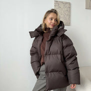 Person wearing a dark brown puffer jacket in a minimal indoor setting