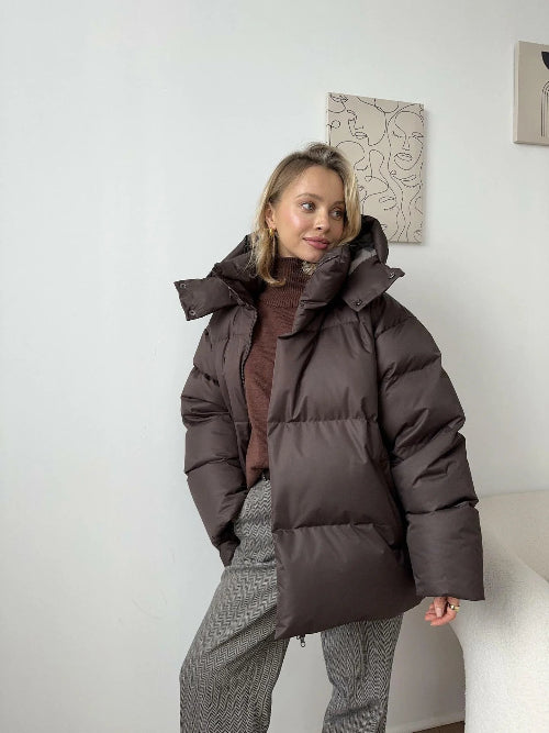 Person wearing a dark brown puffer jacket in a minimal indoor setting