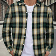 A man wearing a green and beige plaid button-down shirt over a white t-shirt and blue jeans, standing on a city street.