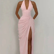 Woman wearing a pink halter neck gown with a high slit on a plain background
