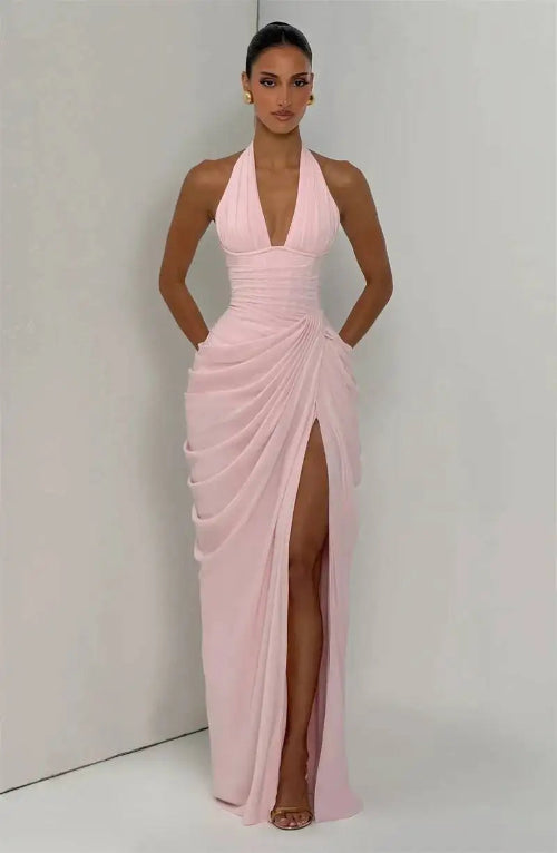 Woman wearing a pink halter neck gown with a high slit on a plain background