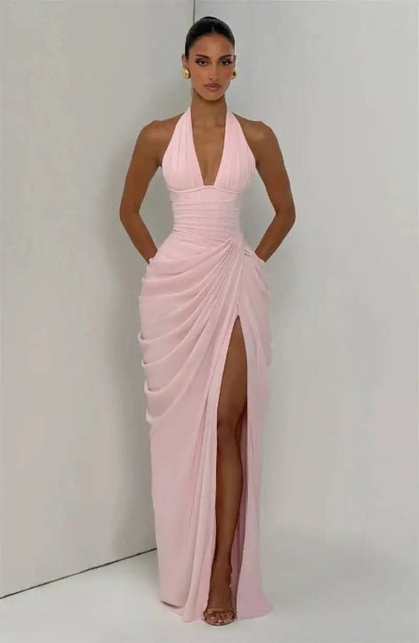 Woman wearing a pink halter neck gown with a high slit on a plain background