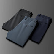 Three pairs of folded men's dress pants in dark gray, charcoal blue, and navy blue, arranged diagonally on a dark gray gradient background.