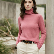 A close-up of a woman wearing a bright pink turtleneck sweater, paired with a black belt featuring a gold double-G buckle.