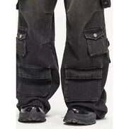 Close-up of washed black baggy cargo jeans showing buttoned side pockets, large lower-leg flap pockets, and wide hems over chunky black shoes.⠋