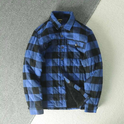 A blue and black buffalo plaid quilted overshirt jacket with a fleece lining, laid flat on a textured gray and white background.