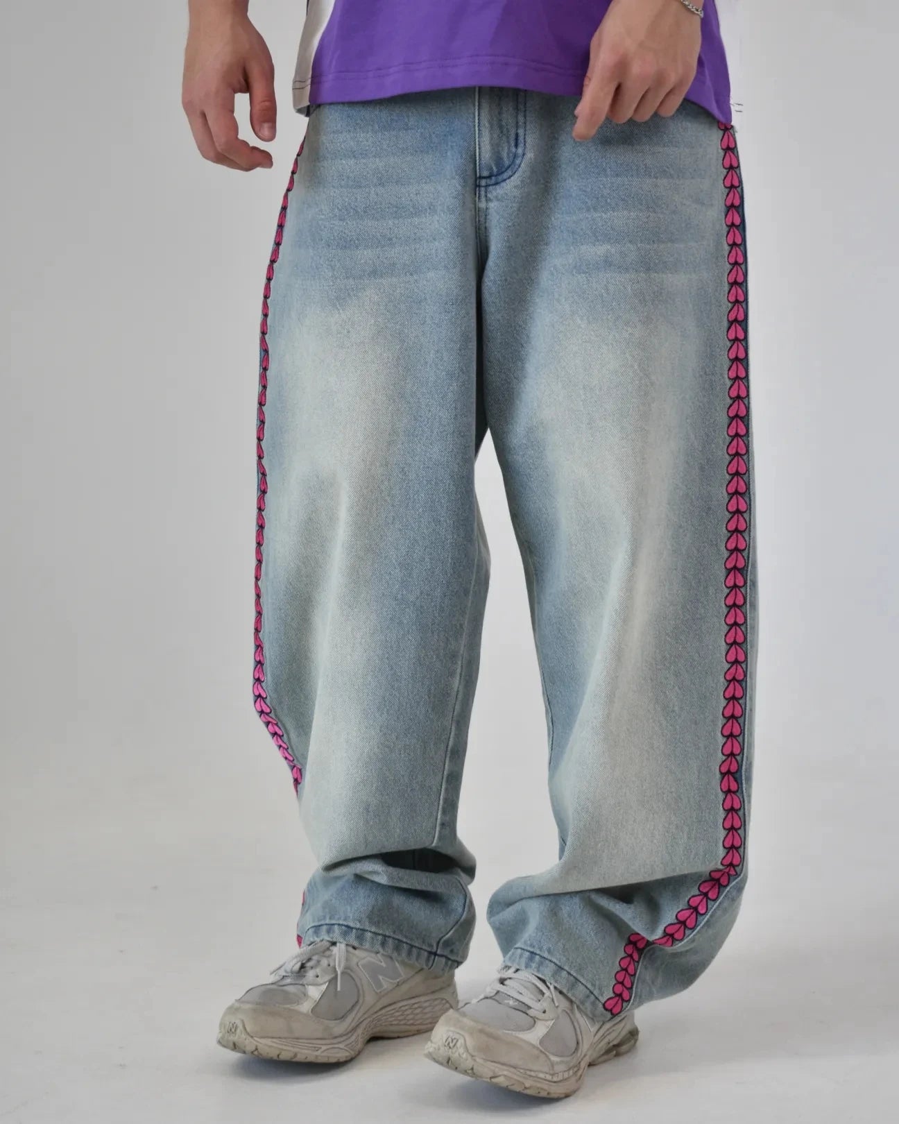 Light blue jeans with pink stitching worn by a person on a plain background