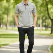 Light gray shirt with a brand logo on a hanger and being held by a hand.