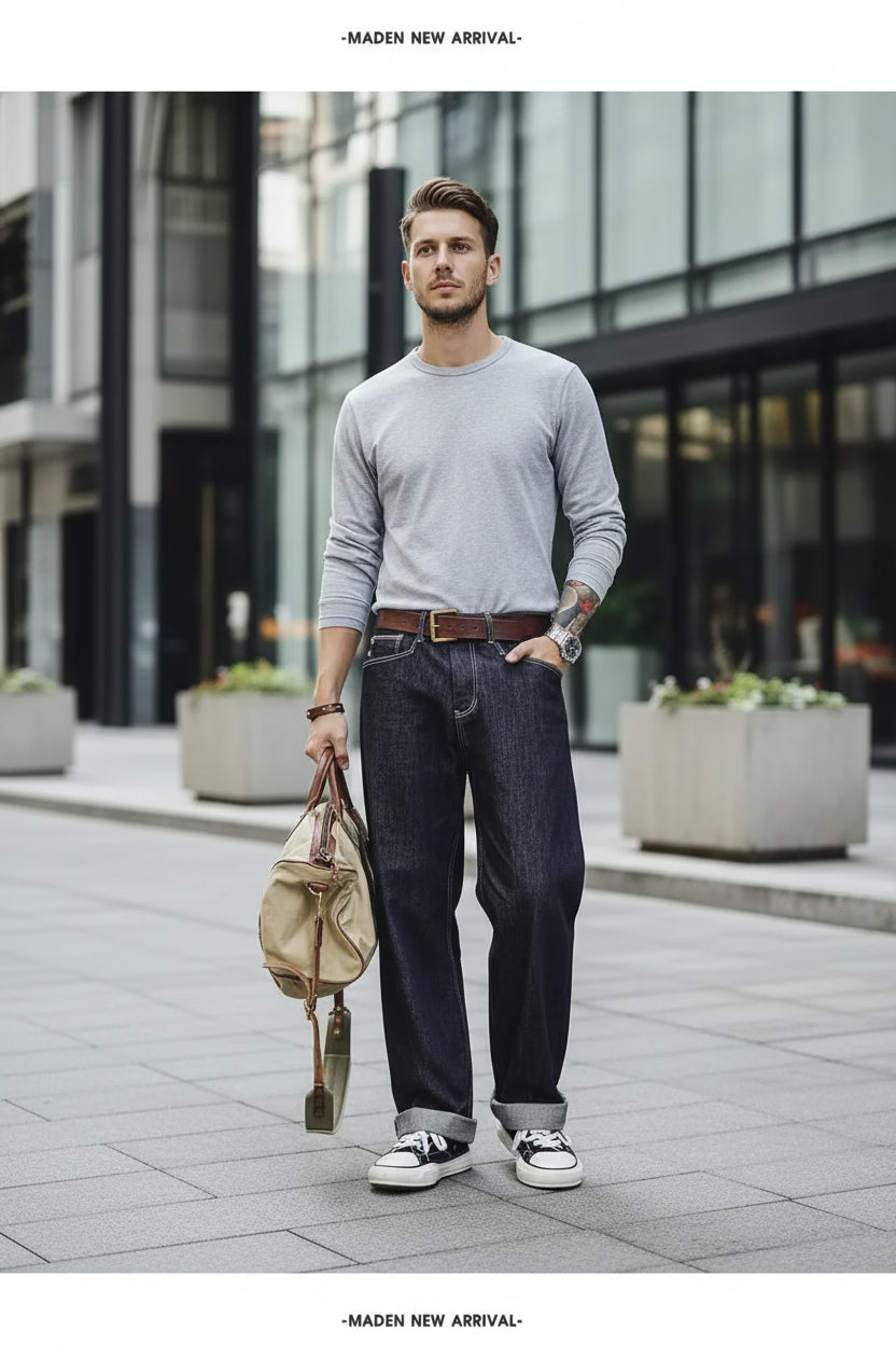 Person wearing blue jeans and a gray sweater, holding a beige handbag, standing in front of a wooden door.