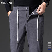 A close-up of a person wearing dark gray textured drawstring trousers with a front zipper and button closure, paired with a black sweater. The brand name MINGYU 