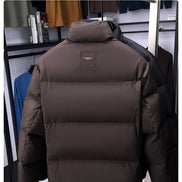 A dark brown puffer jacket displayed on a hanger stand in a retail setting, with a small rectangular brand patch on the upper back. The image includes a light gray header at the top with the text 'SAMPLE SHOW Sample display'.