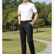 Person wearing black dress pants with a brown belt and shoes on a gray background