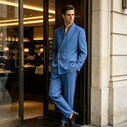 A man wearing a tailored blue double-breasted suit with a split shawl collar, standing in a doorway of a modern building.