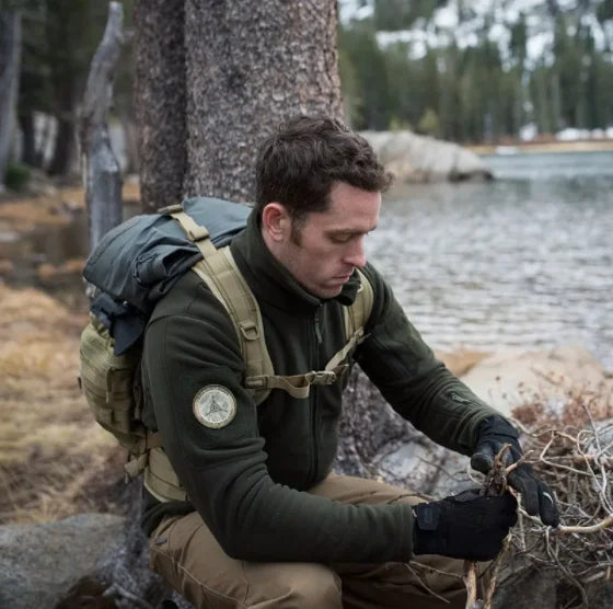 Man in outdoor gear kneeling by a body of water with a backpack