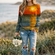 A woman wearing a long-sleeve crewneck sweatshirt with a full-surface sunset and water reflection print, paired with blue jeans and holding a bouquet of white roses.