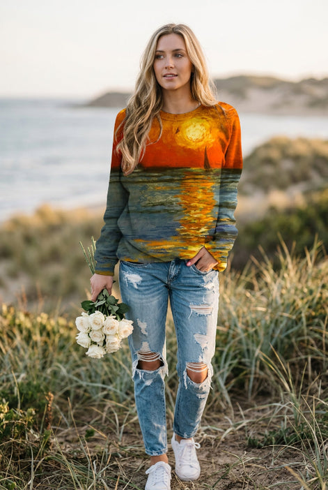 A woman wearing a long-sleeve crewneck sweatshirt with a full-surface sunset and water reflection print, paired with blue jeans and holding a bouquet of white roses.