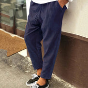 Person wearing navy blue pants and black sneakers leaning against a wall.