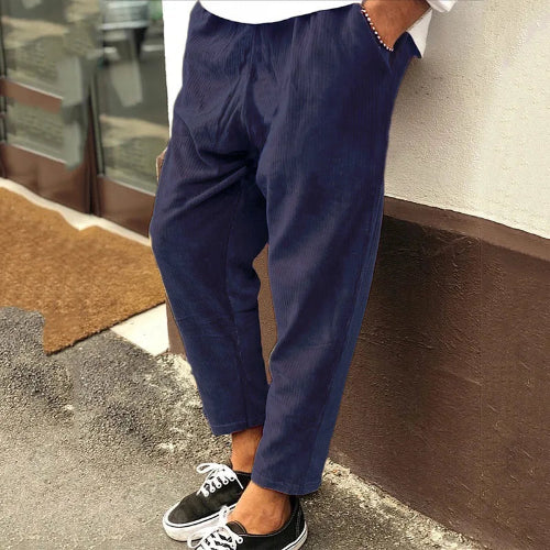 Person wearing navy blue pants and black sneakers leaning against a wall.