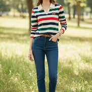 A woman wearing a long-sleeve polo shirt with horizontal stripes in cream, navy, green, and red. The shirt features a solid cream collar and a small brown patch on the left chest.
