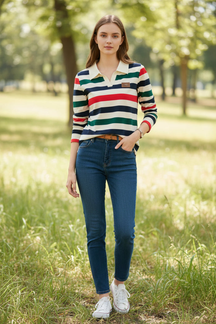 A woman wearing a long-sleeve polo shirt with horizontal stripes in cream, navy, green, and red. The shirt features a solid cream collar and a small brown patch on the left chest.