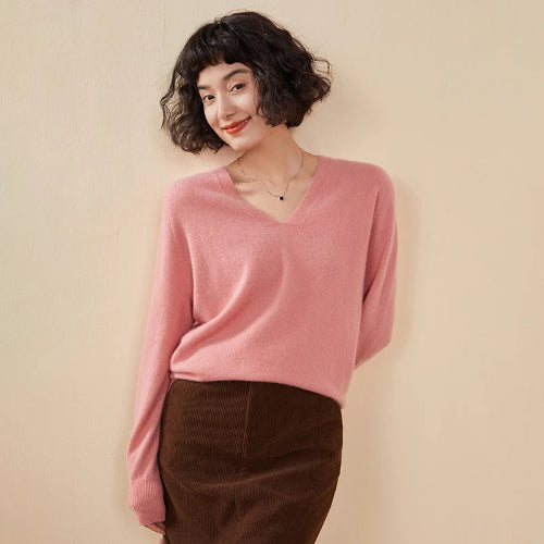 Woman wearing a pink sweater and brown pants against a beige background