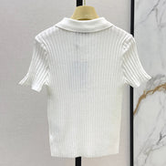 A white short-sleeve ribbed knit polo shirt displayed on a wooden hanger against a light gray wall, with a marble-patterned panel visible on the right.