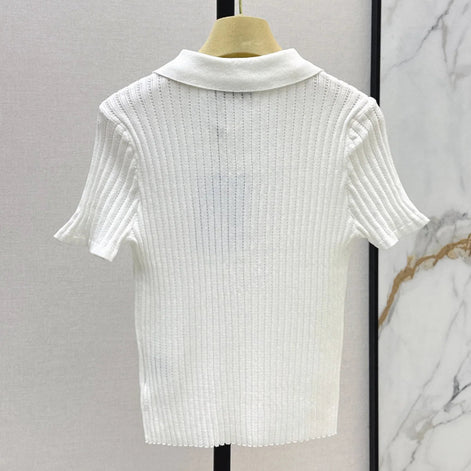 A white short-sleeve ribbed knit polo shirt displayed on a wooden hanger against a light gray wall, with a marble-patterned panel visible on the right.