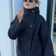 Close-up of a woman wearing a dark double-breasted coat with the stand collar fastened