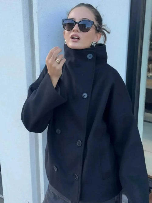 Close-up of a woman wearing a dark double-breasted coat with the stand collar fastened