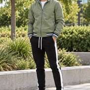 A men's two-piece tracksuit set featuring an olive green zip-up bomber jacket with striped ribbed trim and black track pants 