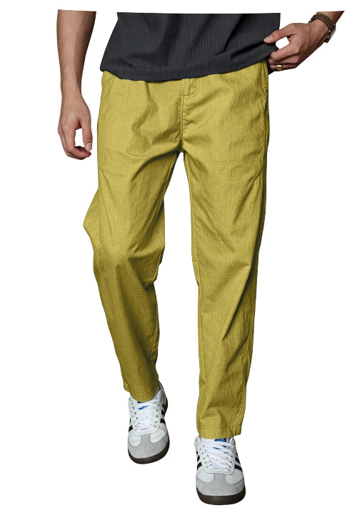 A person wearing slim-fit mustard yellow trousers, a dark gray t-shirt, and white sneakers, shown from the waist down against a plain white background.