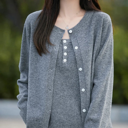 A woman wearing a gray knit cardigan over a matching gray ribbed top, shown from the chest down against a softly blurred outdoor background.