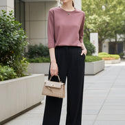 Person wearing a pink top and holding a beige handbag indoors.