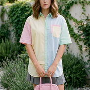 A woman wearing a pastel multicolor raglan t-shirt with pink, yellow, light blue, and mint green panels, standing in a garden setting with a wooden folding chair and potted flowers.