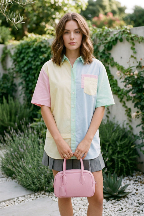 A woman wearing a pastel multicolor raglan t-shirt with pink, yellow, light blue, and mint green panels, standing in a garden setting with a wooden folding chair and potted flowers.