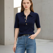 Person wearing a navy blue short-sleeve shirt with gold buttons and blue jeans indoors.