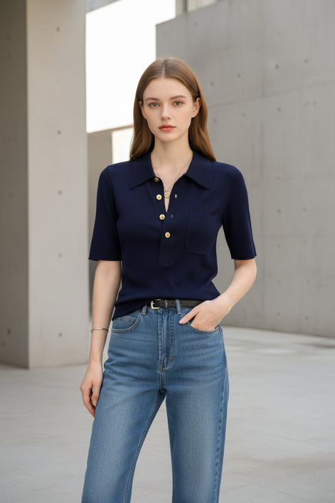 Person wearing a navy blue short-sleeve shirt with gold buttons and blue jeans indoors.