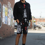 Person wearing black shorts with graphic designs and white sneakers on a white background