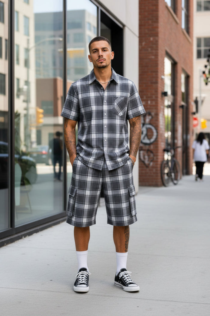 Man wearing a gray plaid shirt and shorts with black Converse shoes taken outside