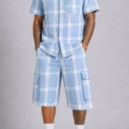 A man modeling a light blue and white plaid short-sleeve button-up shirt and matching cargo shorts, paired with white socks and black sneakers, against a neutral gray studio background.