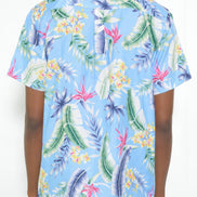A man wearing a light blue short-sleeve button-up shirt with a colorful tropical leaf and floral print, shown from the back against a plain white background.