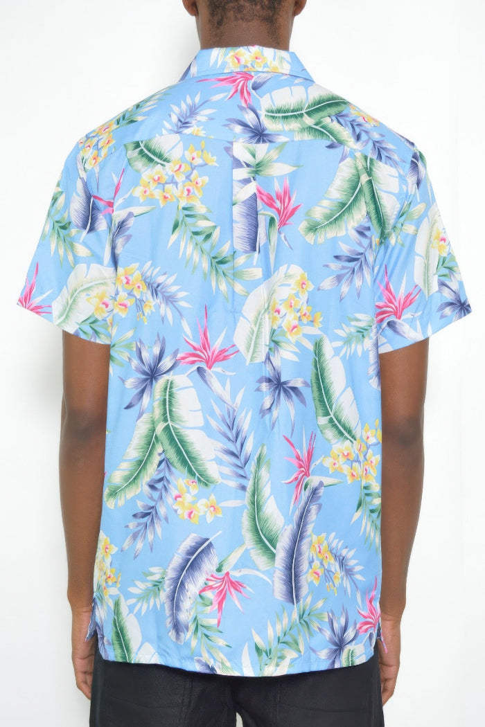 A man wearing a light blue short-sleeve button-up shirt with a colorful tropical leaf and floral print, shown from the back against a plain white background.