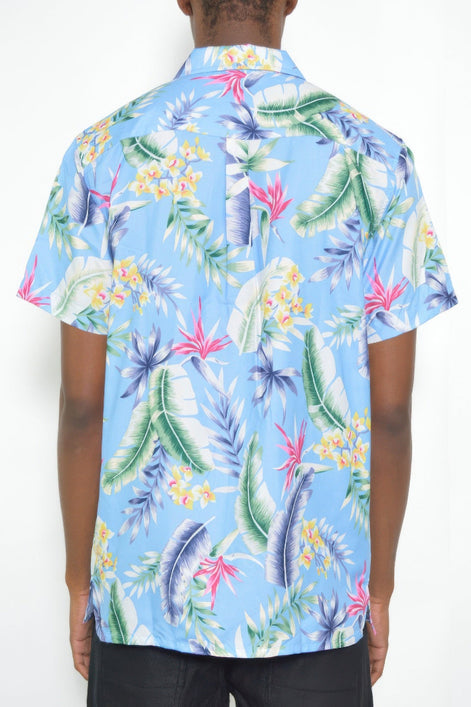 A man wearing a light blue short-sleeve button-up shirt with a colorful tropical leaf and floral print, shown from the back against a plain white background.