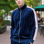 Man wearing a blue velvet tracksuit with white stripes  taken outside