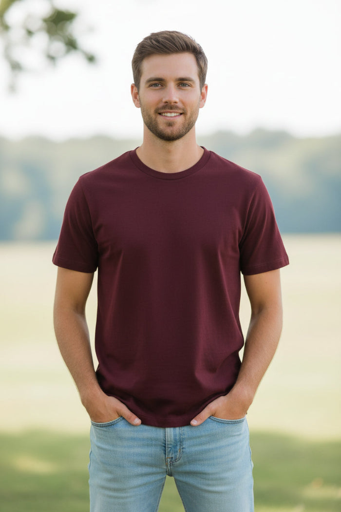 A man wearing a solid maroon crew-neck t-shirt and light blue jeans, shown from the chin down against a plain white background.