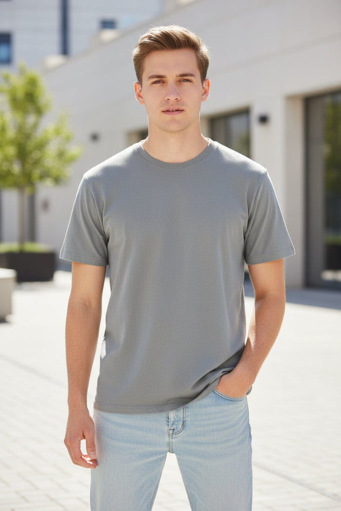 A man wearing a plain light gray crew-neck t-shirt and light blue jeans, shown from the chin down against a white studio background.