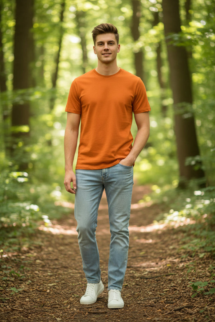 A man wearing a solid orange crew-neck t-shirt and light blue jeans, shown from the chin down against a plain white background.